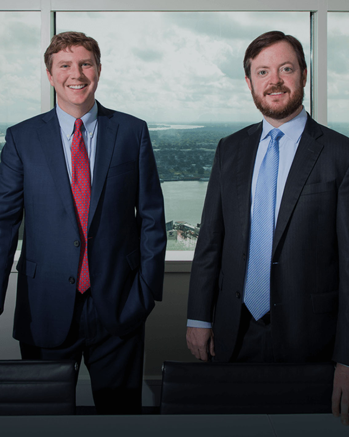 Two attorneys in suits, Lance McCardle and Jason W. Burge, stand in front of high rise office window with view of river below